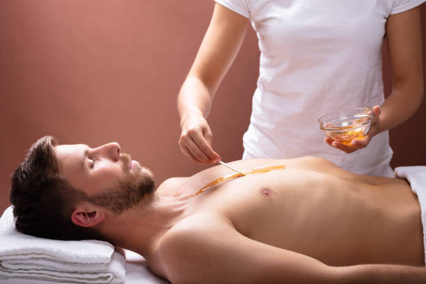 Close-up Of Therapist Hand Applying Wax On Relaxed Young Man’s Chest